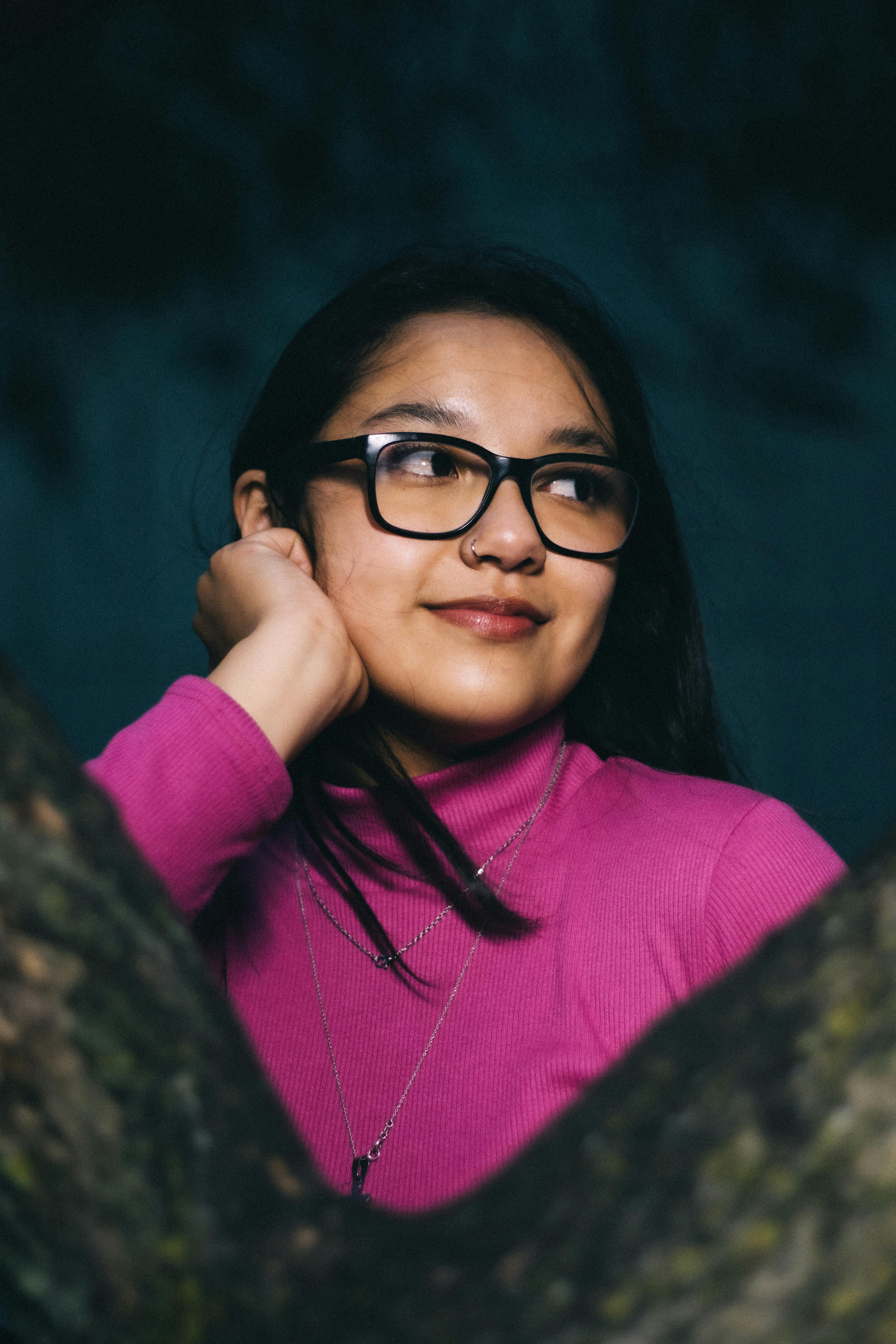 Portrait of a smiling woman wearing glasses and a pink sweater, captured outdoors in a natural setting.