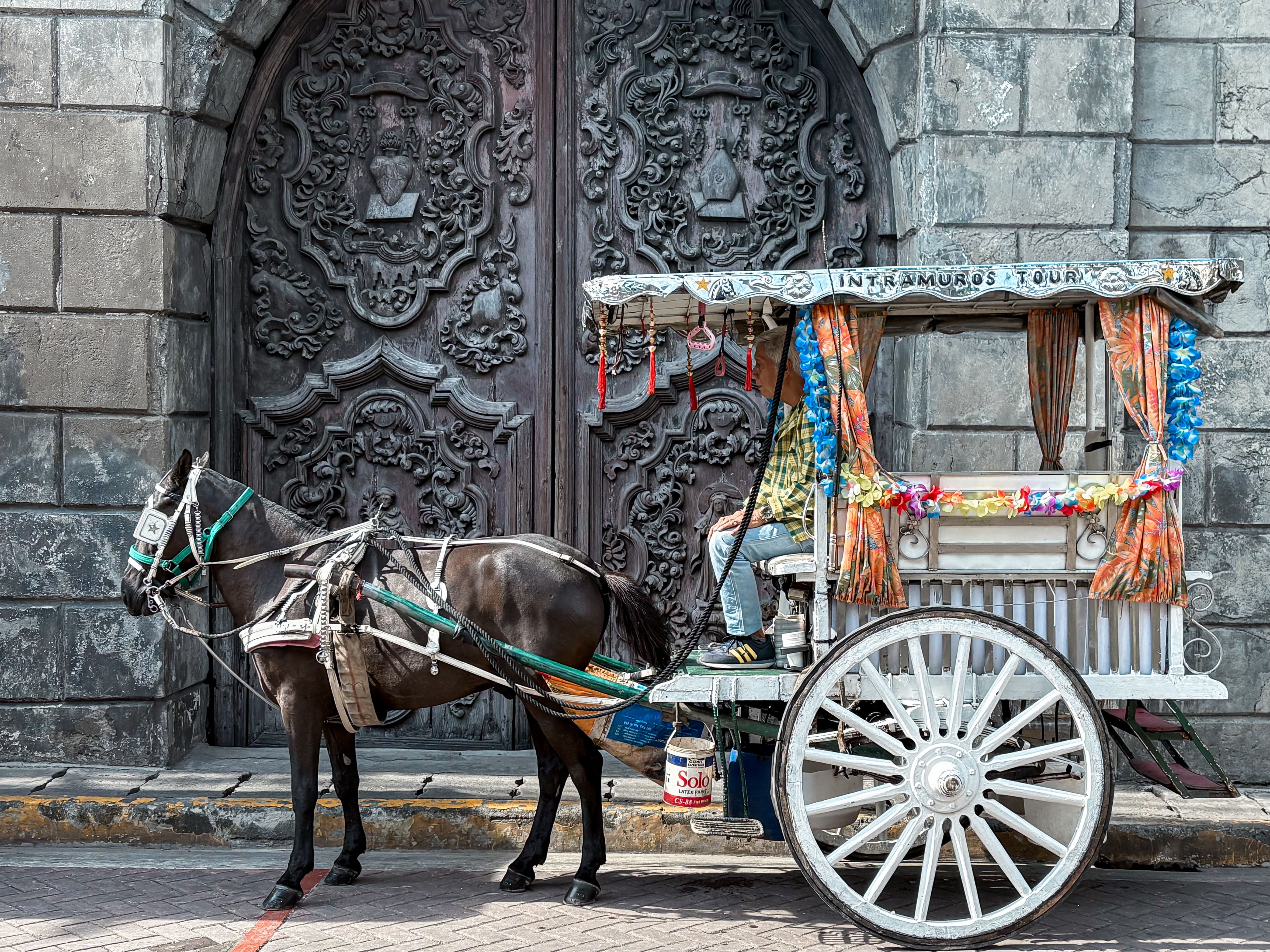 Decorative horse-drawn carriage parked in front of ornate stone gate in Manila. - Manila