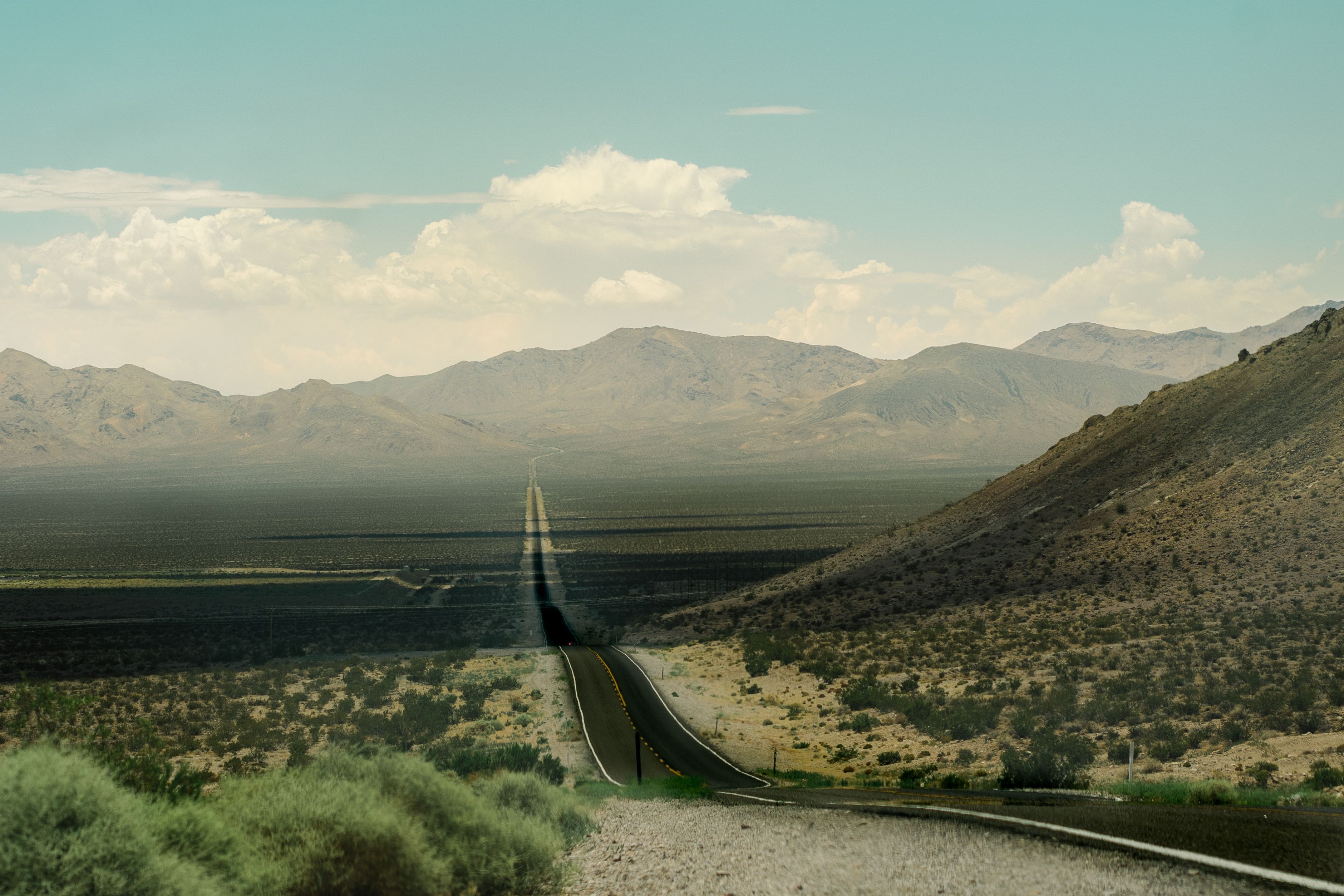 A straight road stretches through the arid California desert under a clear sky, offering a sense of adventure.
