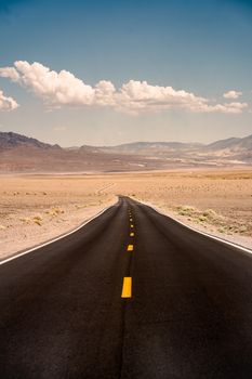 A scenic road stretches through the desert landscape towards distant mountains under a blue sky.