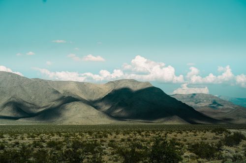Free A breathtaking view of a desert landscape with majestic mountains casting shadows under a bright sky. Stock Photo