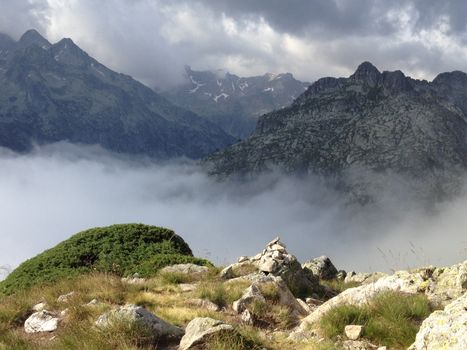 Observe the breathtaking mountain panorama with low clouds and rugged peaks, capturing a serene natural beauty.