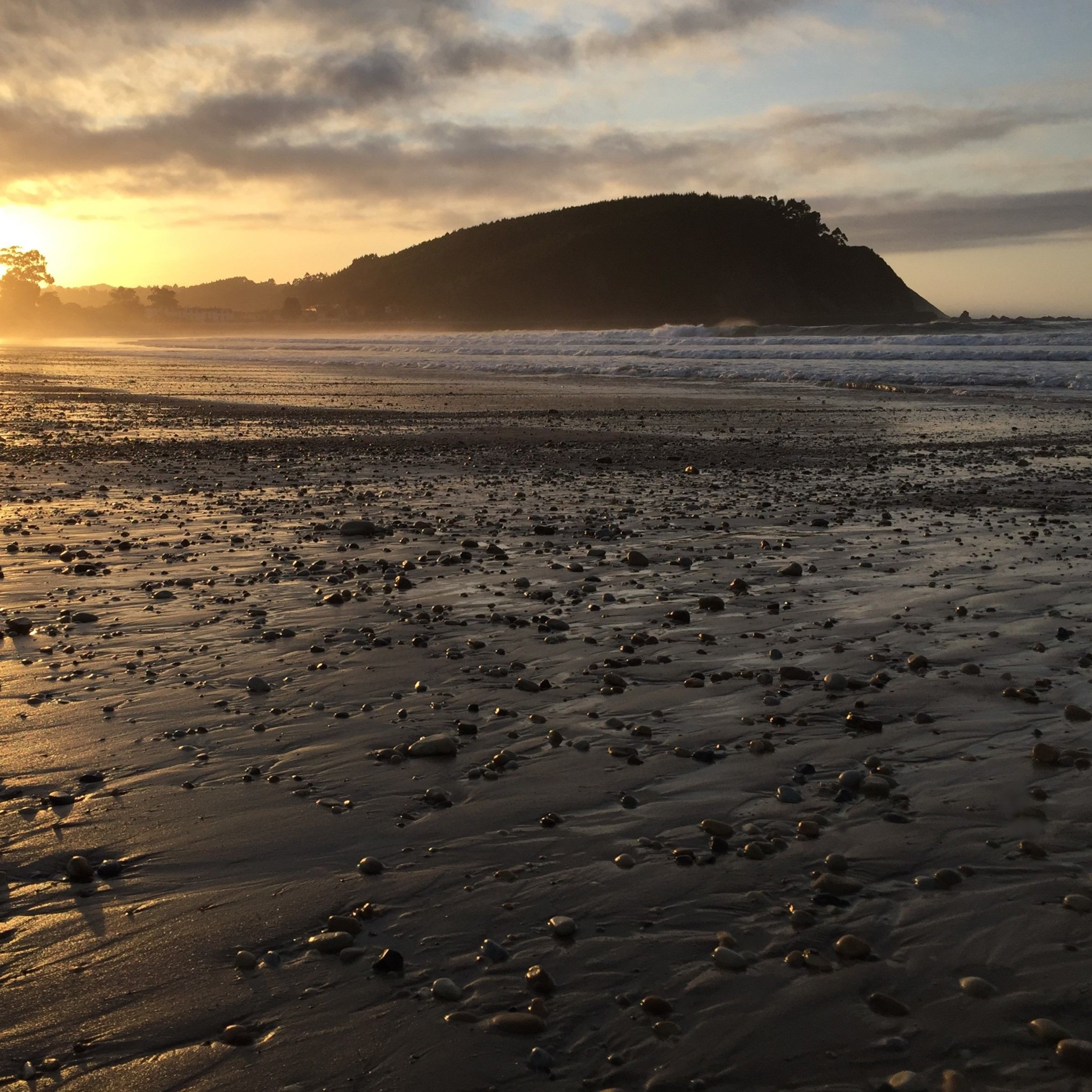 A tranquil sunset over a Spanish beach with golden reflections and a mountainous horizon.