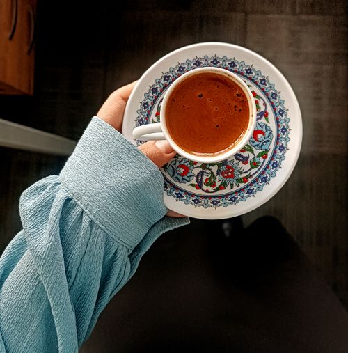 Free Hand holding an intricately designed cup of Turkish coffee with floral patterns on a saucer. Stock Photo