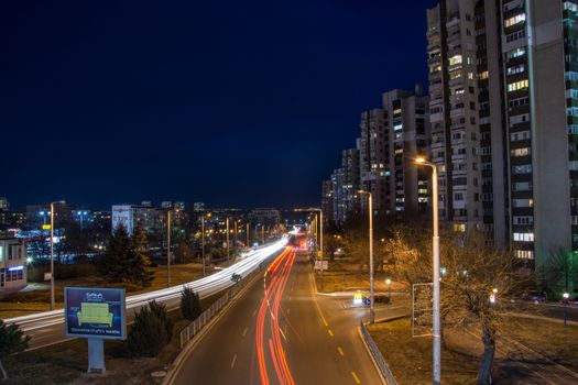 City road at night with light streaks and illuminated buildings showcasing urban dynamic life.