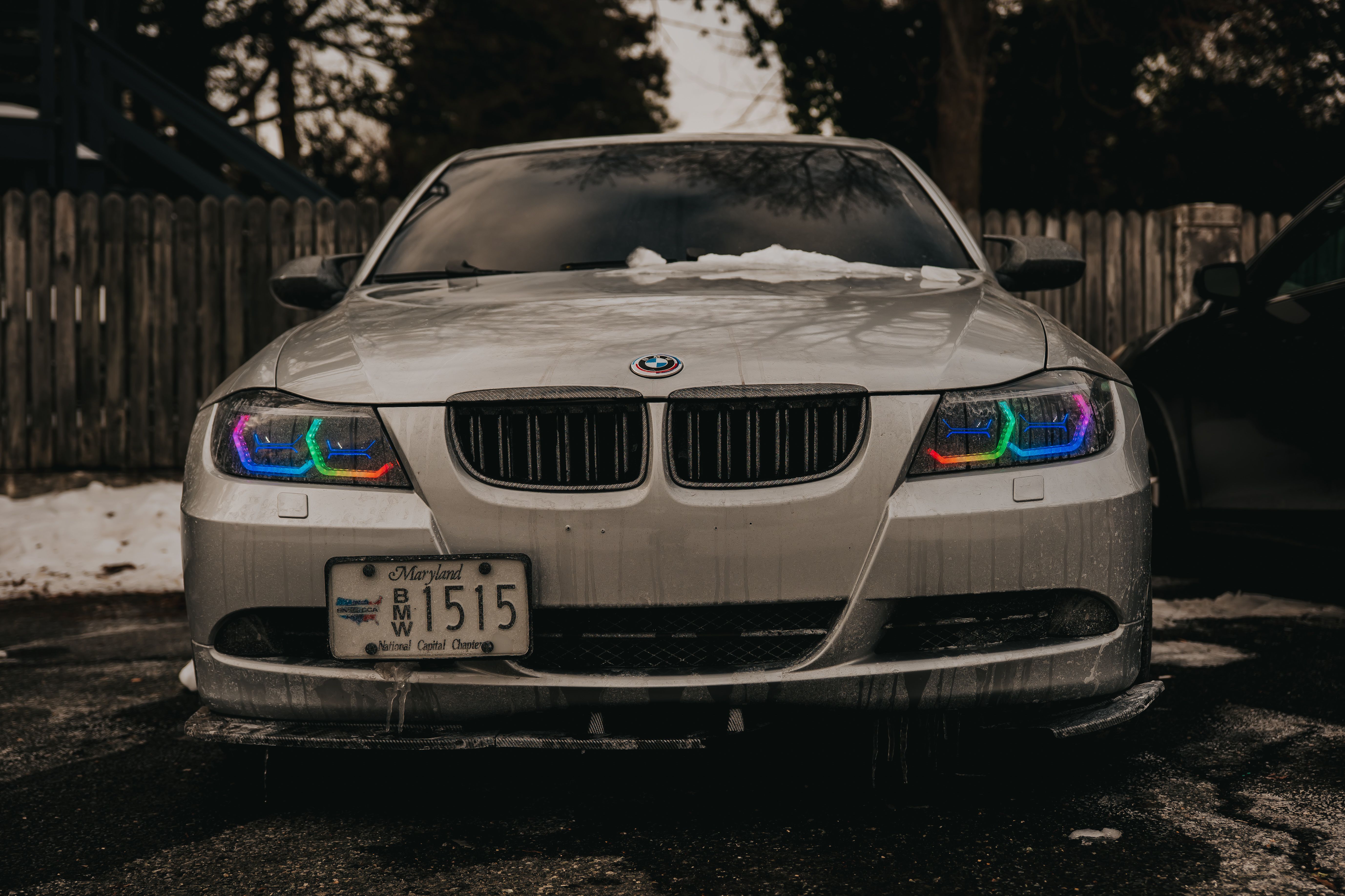 Front view of a BMW with vibrant, custom rainbow headlights, parked on a snowy day.