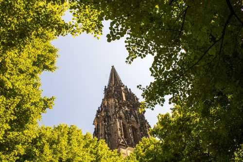 Free St. Nikolai Church spire in Hamburg, Germany, framed by lush summer foliage, showcasing Gothic architecture. Stock Photo