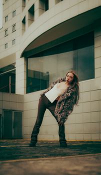Stylish woman in urban setting showcasing fashion with modern architecture backdrop.