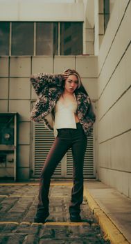 Woman in fashionable attire poses confidently in an urban alleyway, showcasing modern street fashion.