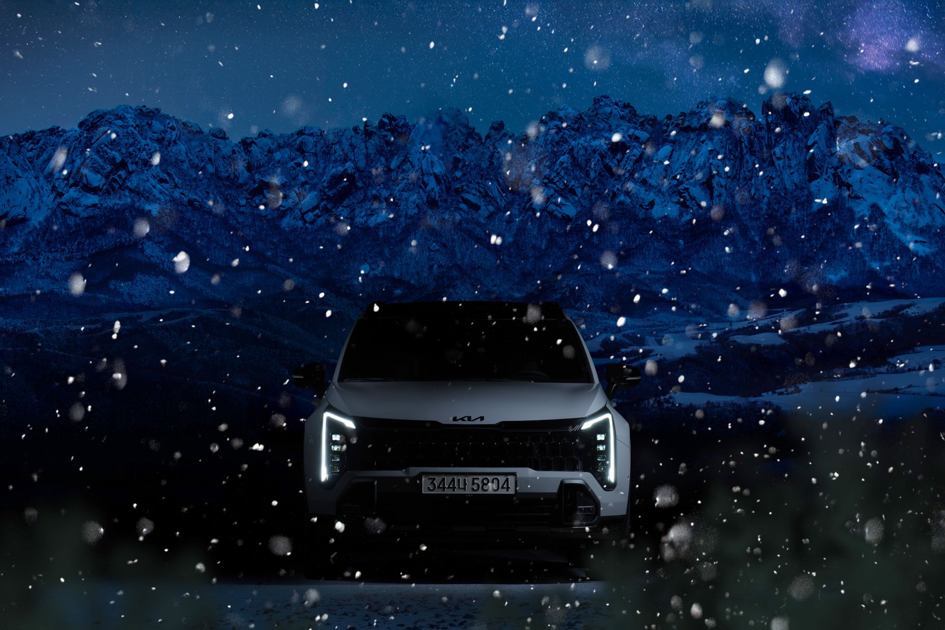 A Kia SUV navigates through snowy mountains under a starry night sky.