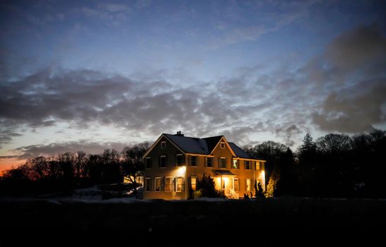 A cozy house illuminated at twilight surrounded by a serene winter landscape.