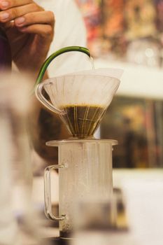Artistic shot of a barista pouring water into a V60 dripper with focus on the brewing process.