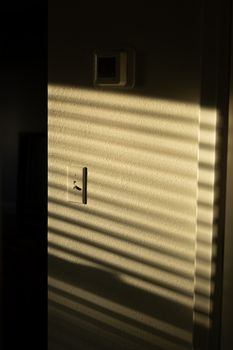 A wall with shadows from window blinds at sunrise, creating a warm abstract pattern.