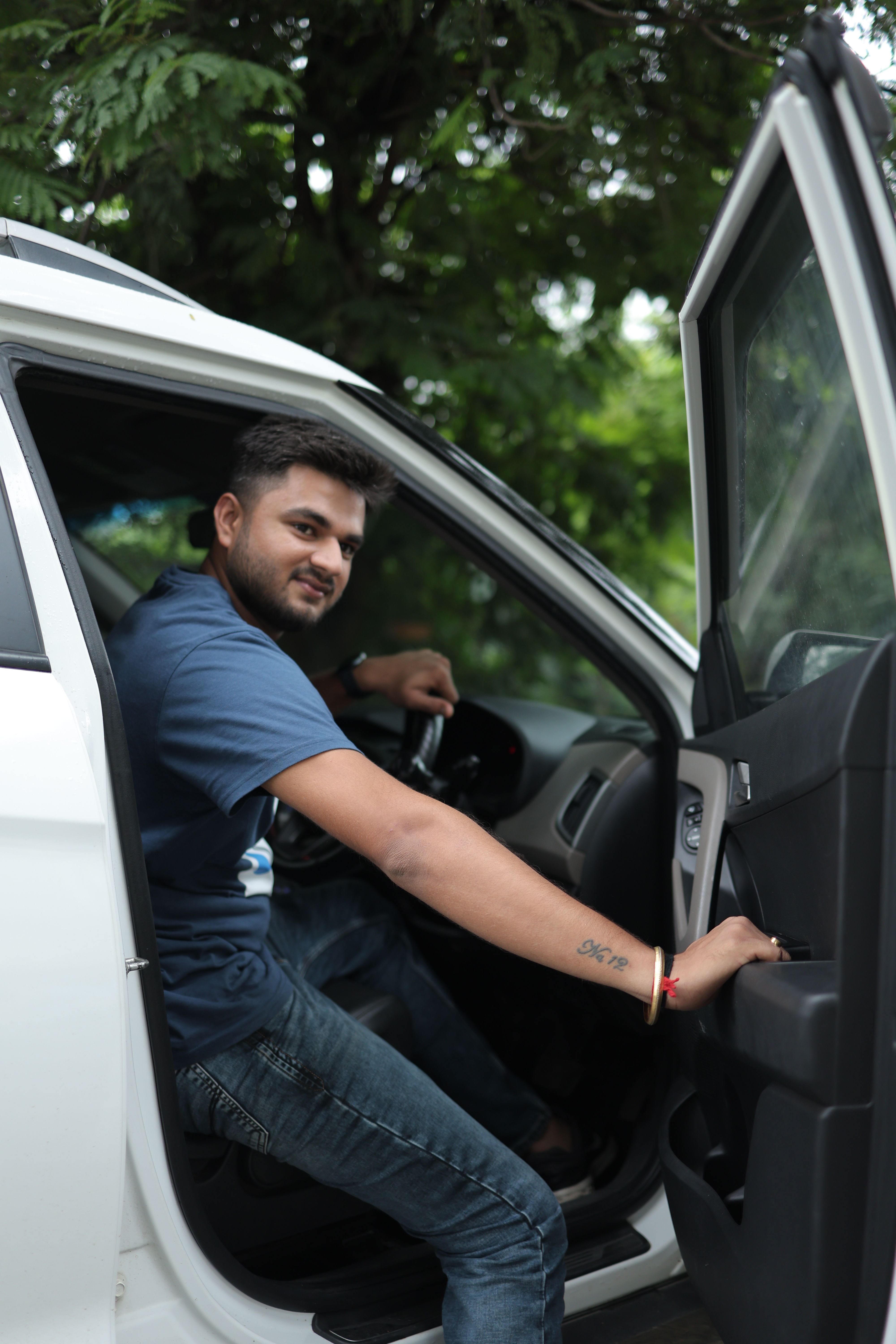 Portrait of a man exiting a car with greenery in the background, captured in a candid moment.