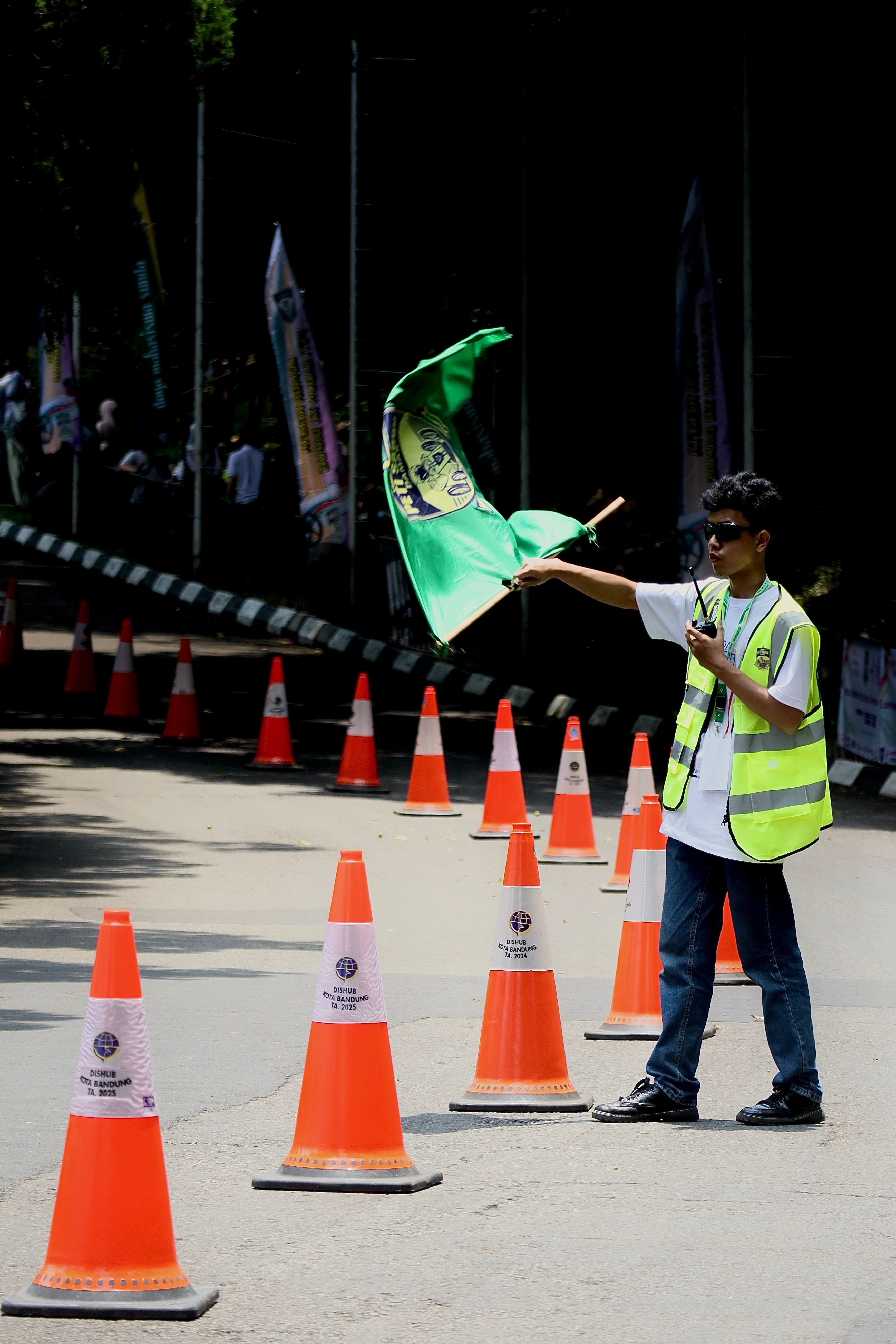 Race official with green flag directing vehicles outdoors near traffic cones.