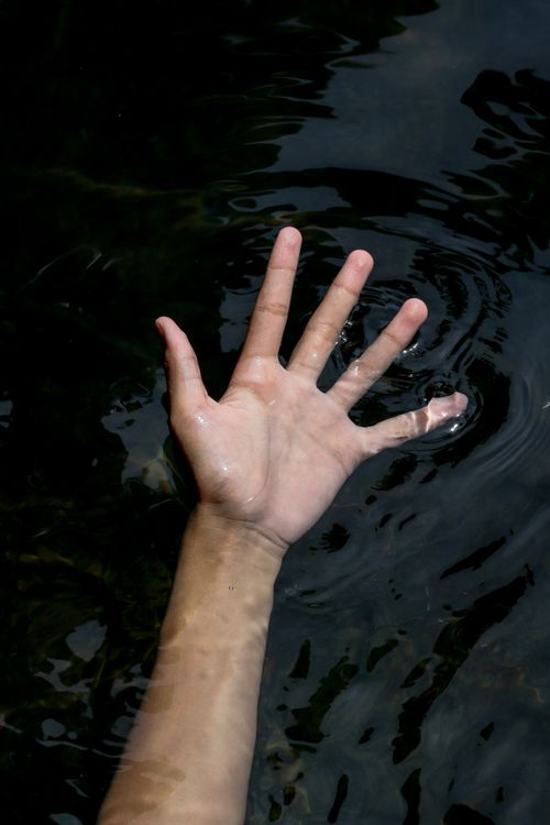 Free A hand partially submerged in dark water, creating a dramatic and expressive scene. Stock Photo