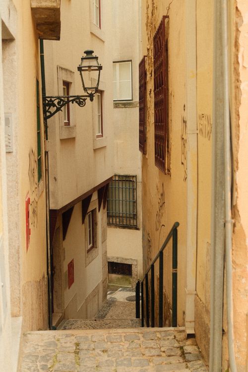 Free Explore Lisbon's historic charm with this narrow alleyway scene featuring traditional architecture and warm tones. Stock Photo