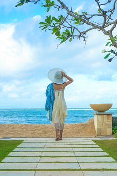 A woman in a sun hat overlooks the tranquil Bali seascape, capturing the essence of relaxation and tropical beauty.