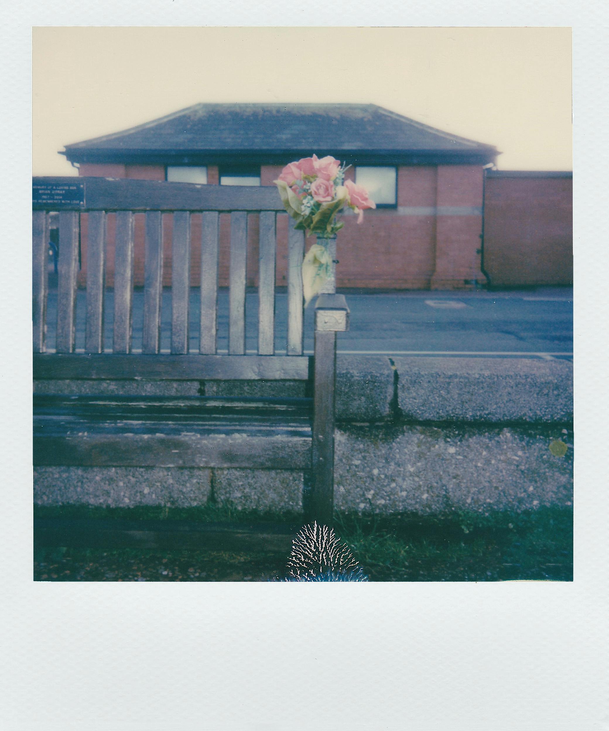 Vintage instant photo of a rustic bench with a floral bouquet in an urban environment.