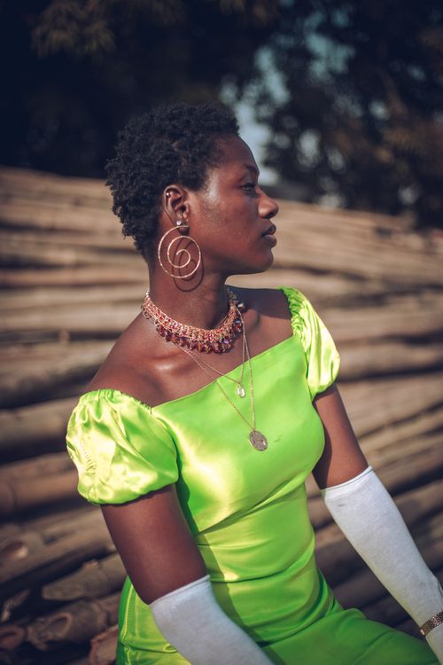 Free Side profile of a stylish woman in a neon green dress and jewelry against a rustic background. Stock Photo