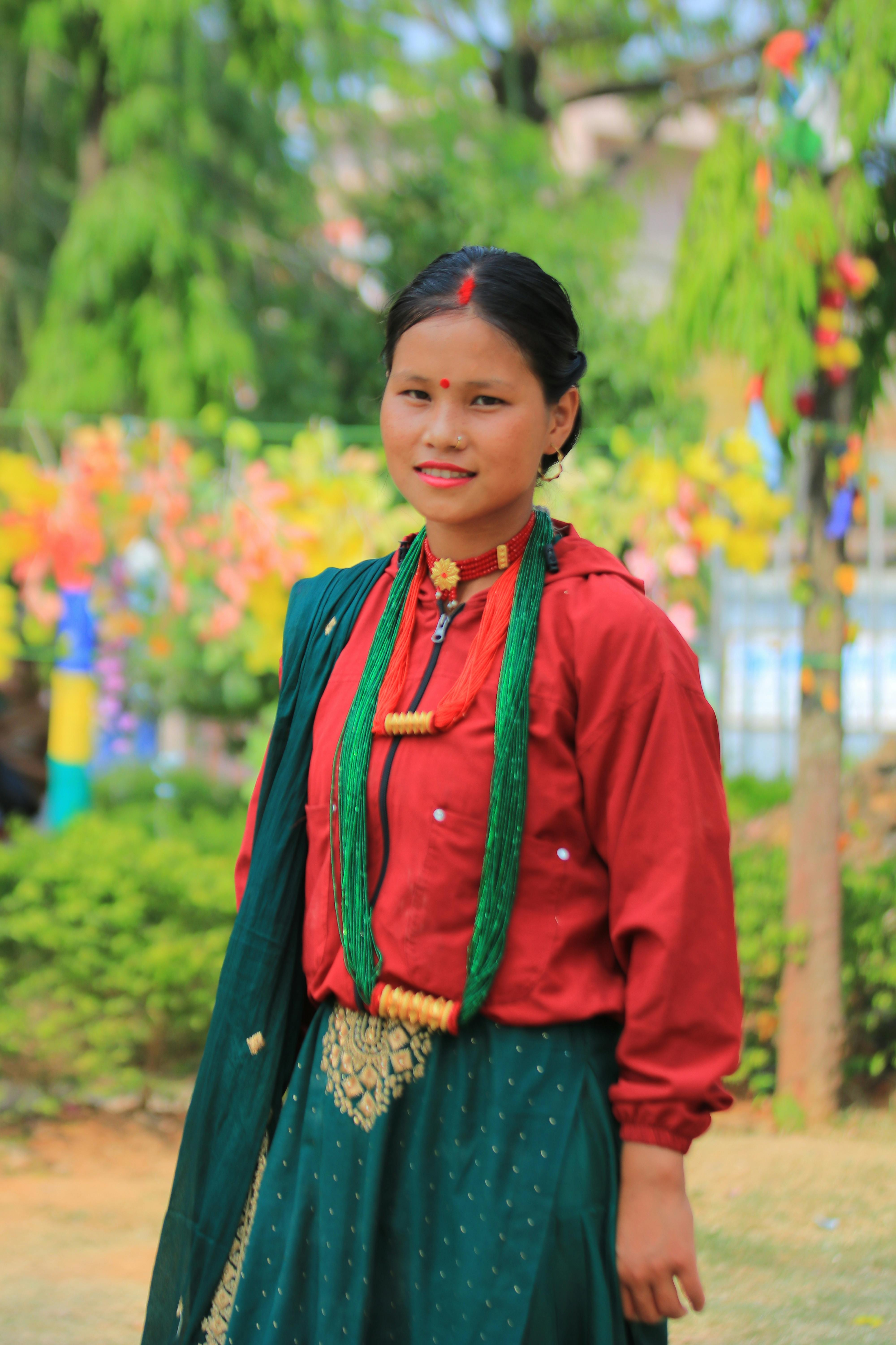 A woman in traditional clothing smiles in a vibrant outdoor setting, showcasing cultural attire.