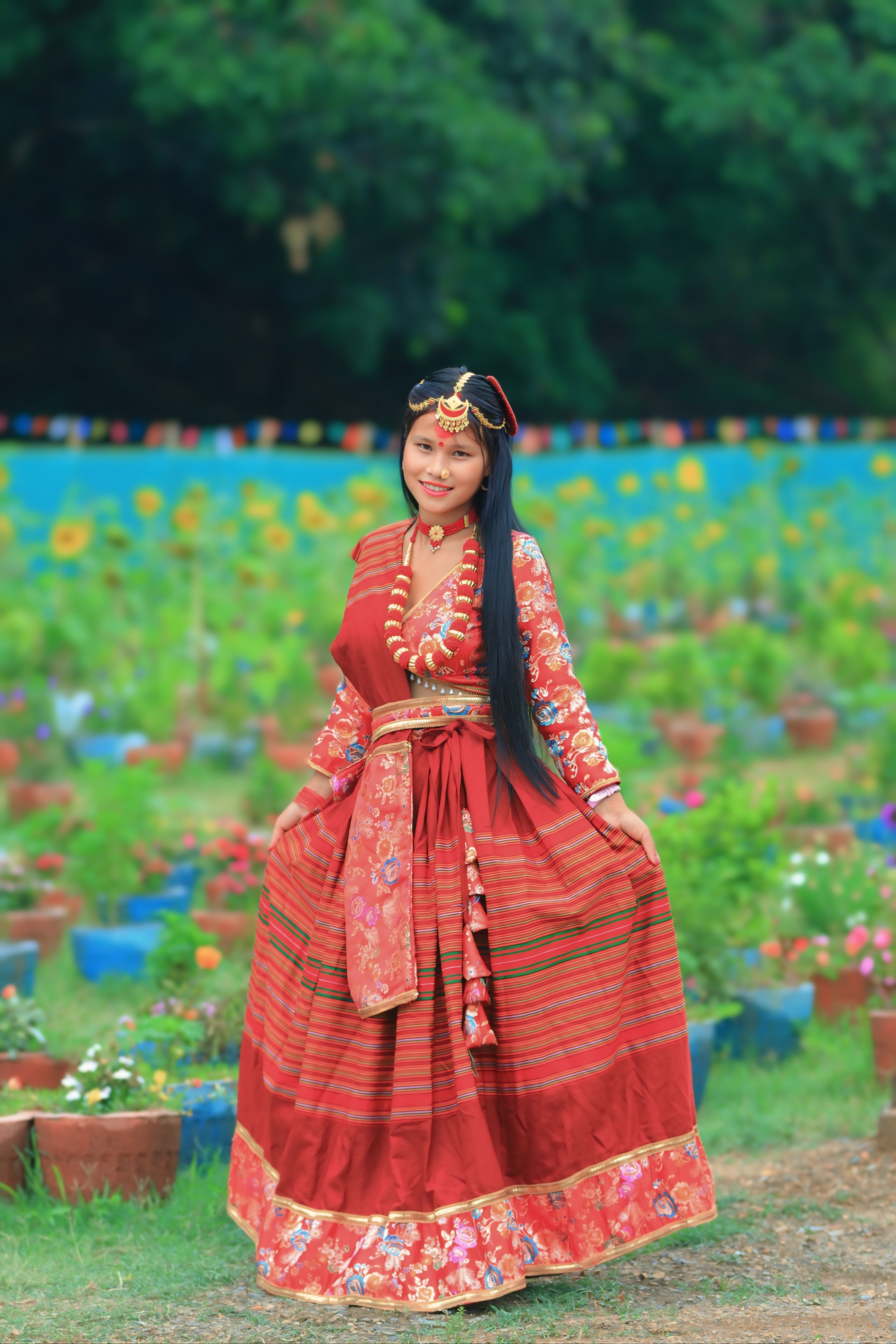 Woman in vibrant traditional dress posing in colorful garden setting with flowers.