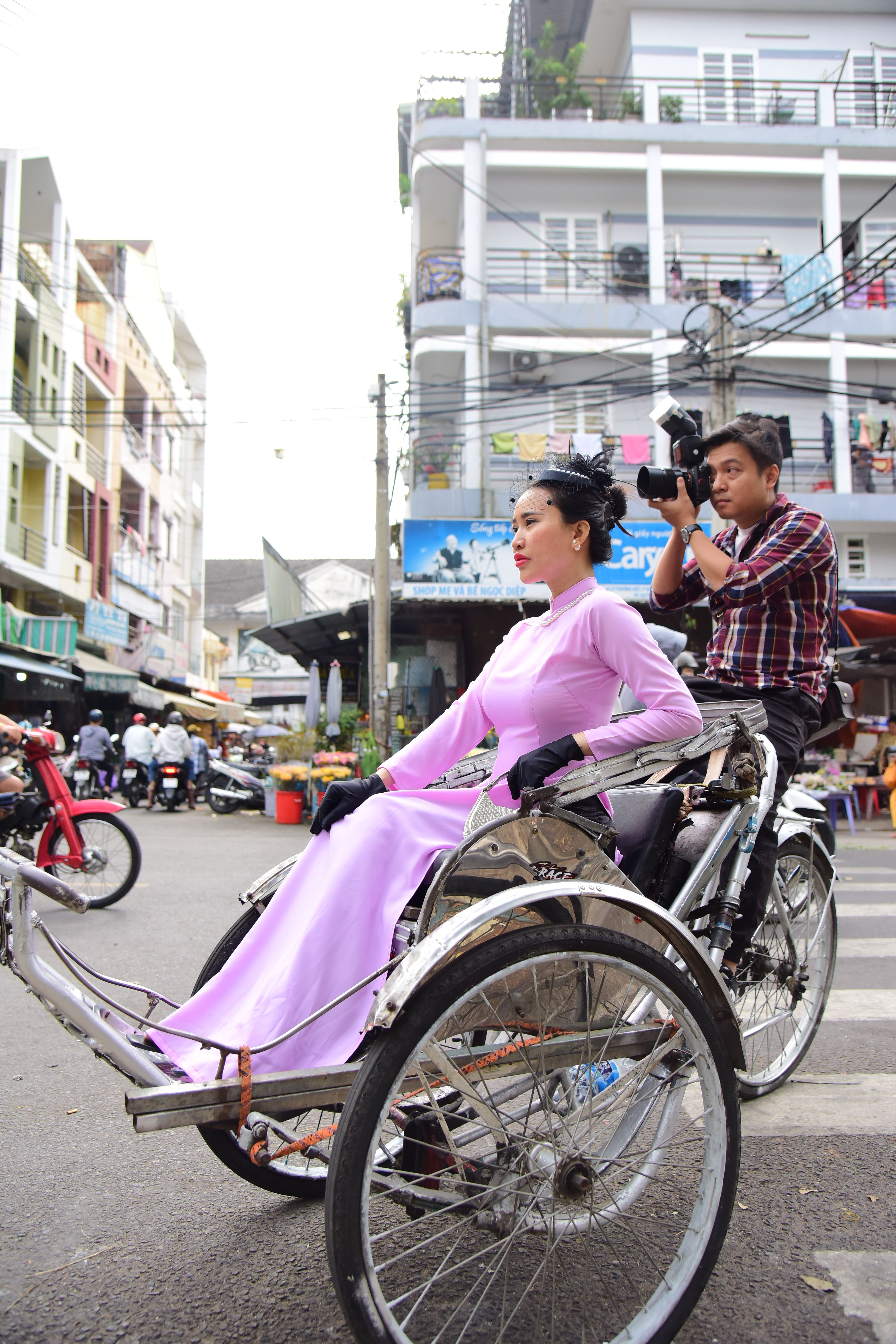 A woman in traditional attire poses on a rickshaw in a bustling city street.