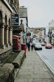 老城街景热闹非凡，行人、汽车和传统的红色电话亭点缀其间