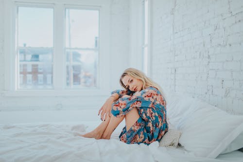 Wanita Mengenakan Gaun Bermotif Bunga Saat Duduk Di Tempat Tidur