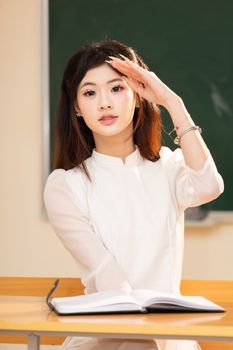 Portrait of a young woman in a classroom, Hanoi, wearing traditional Vietnamese ao dai.