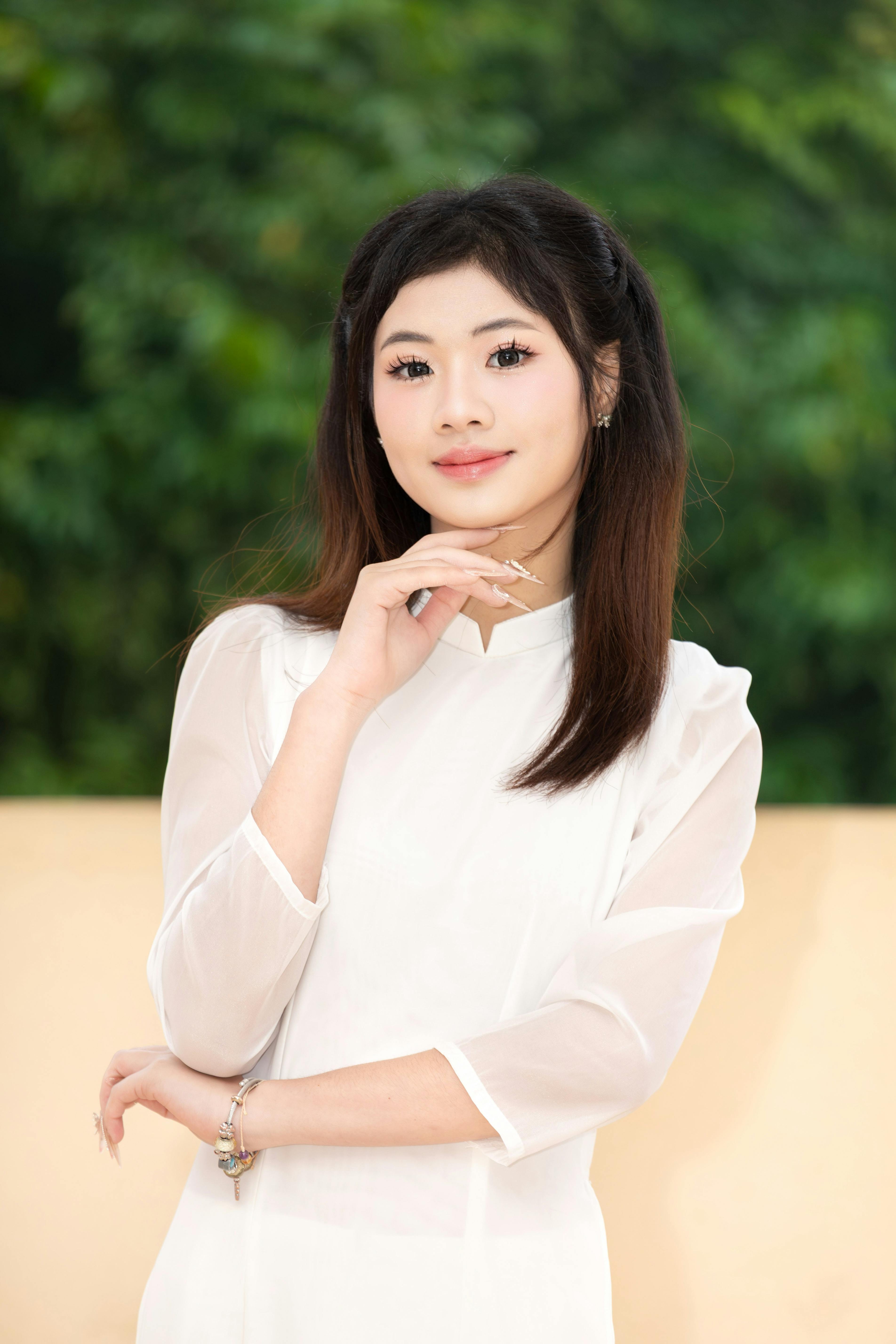 Portrait of a young woman in a white áo dài, standing outdoors in Hanoi, Vietnam.