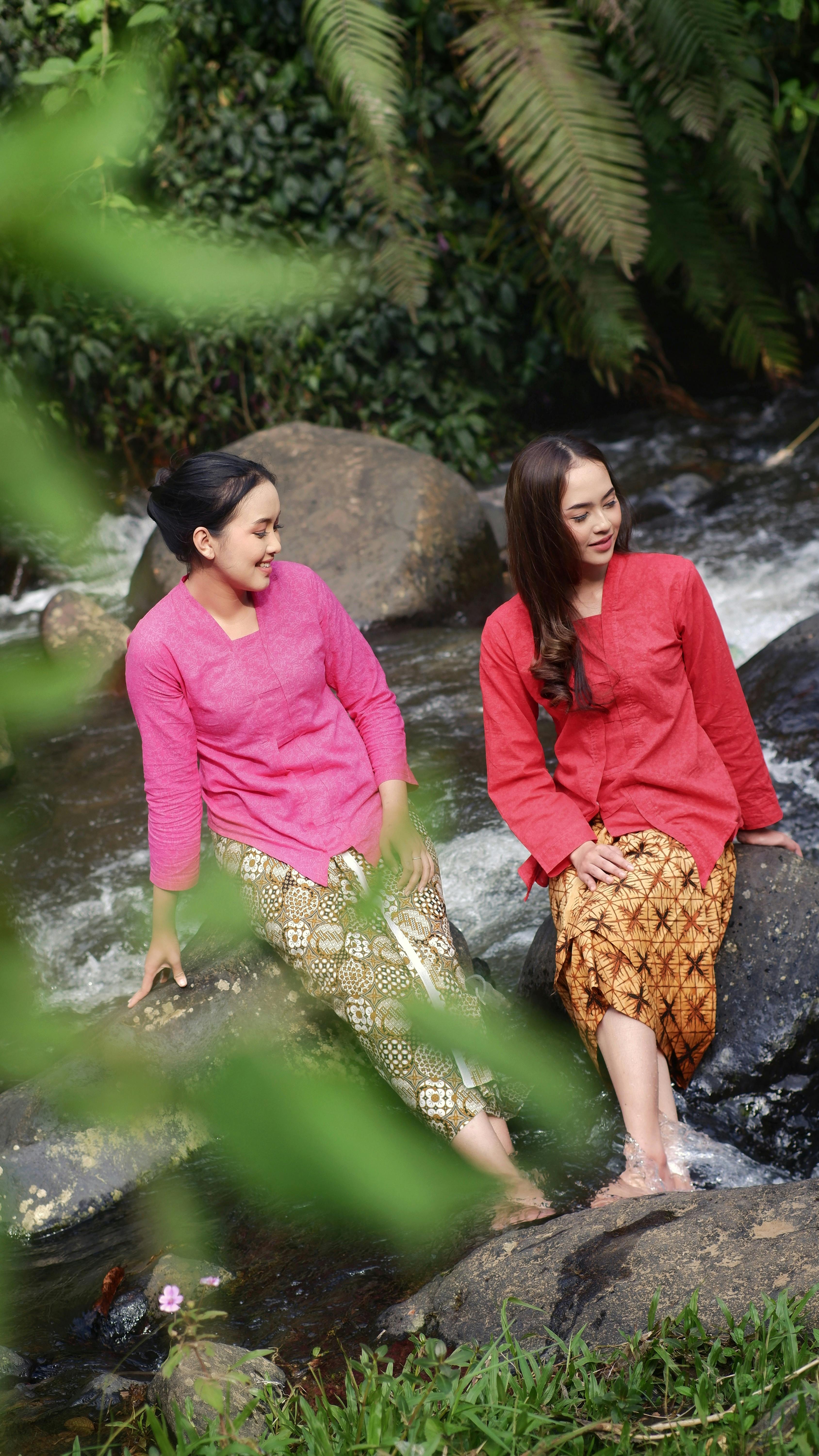 Two women in traditional attire enjoying a serene moment by a stream in West Java.