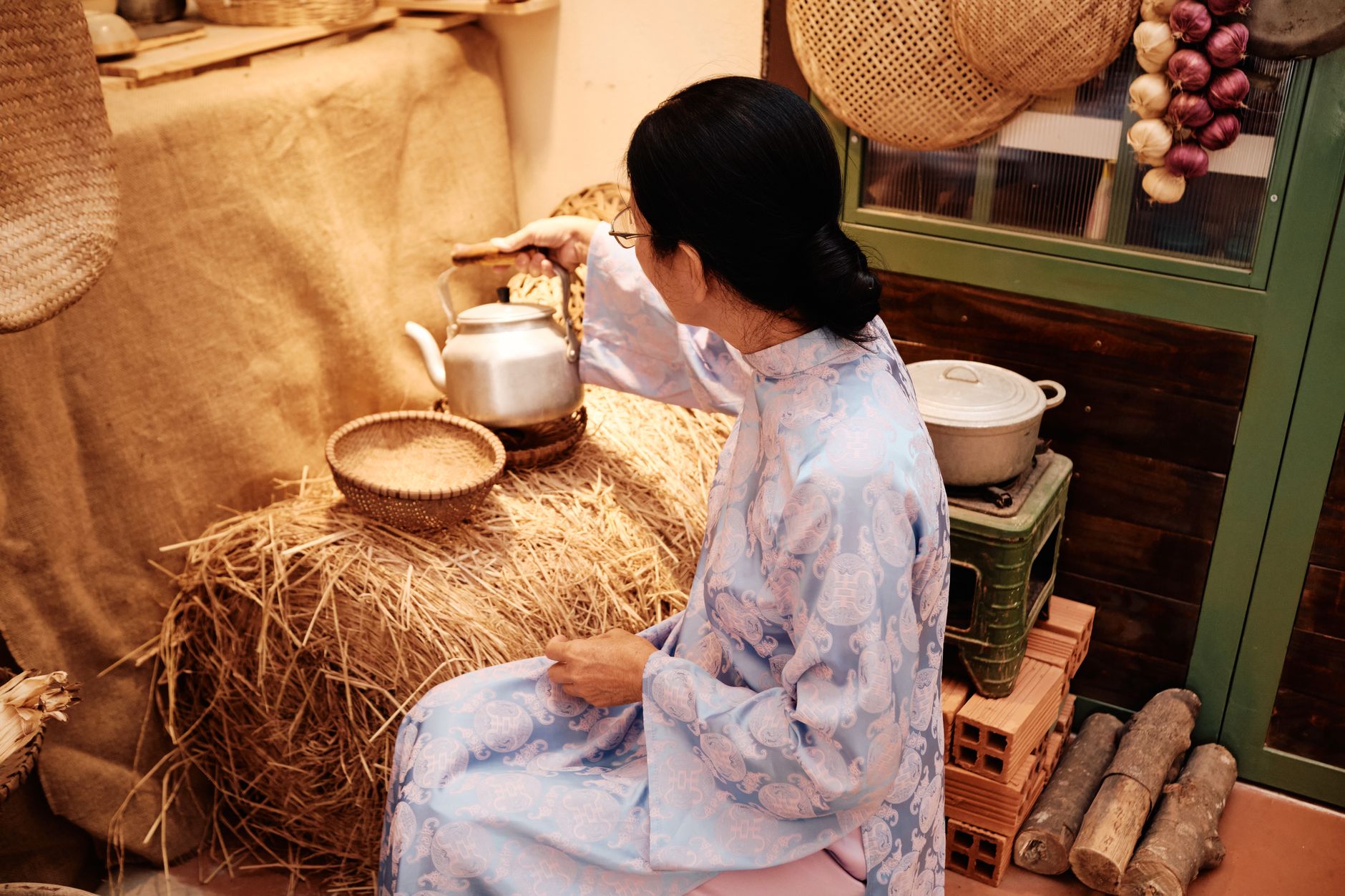 A woman in traditional attire making tea in a rustic setting in Vietnam.