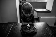 一个小男孩若有所思地看着生日蛋糕，蜡烛被拍成了黑白色
