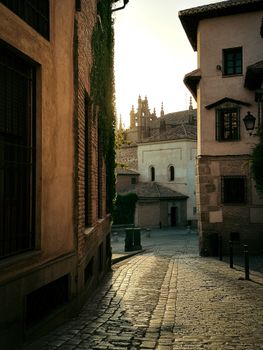 Charming alleyway with cobblestone path leading to Toledo Cathedral in Spain during sunset.
