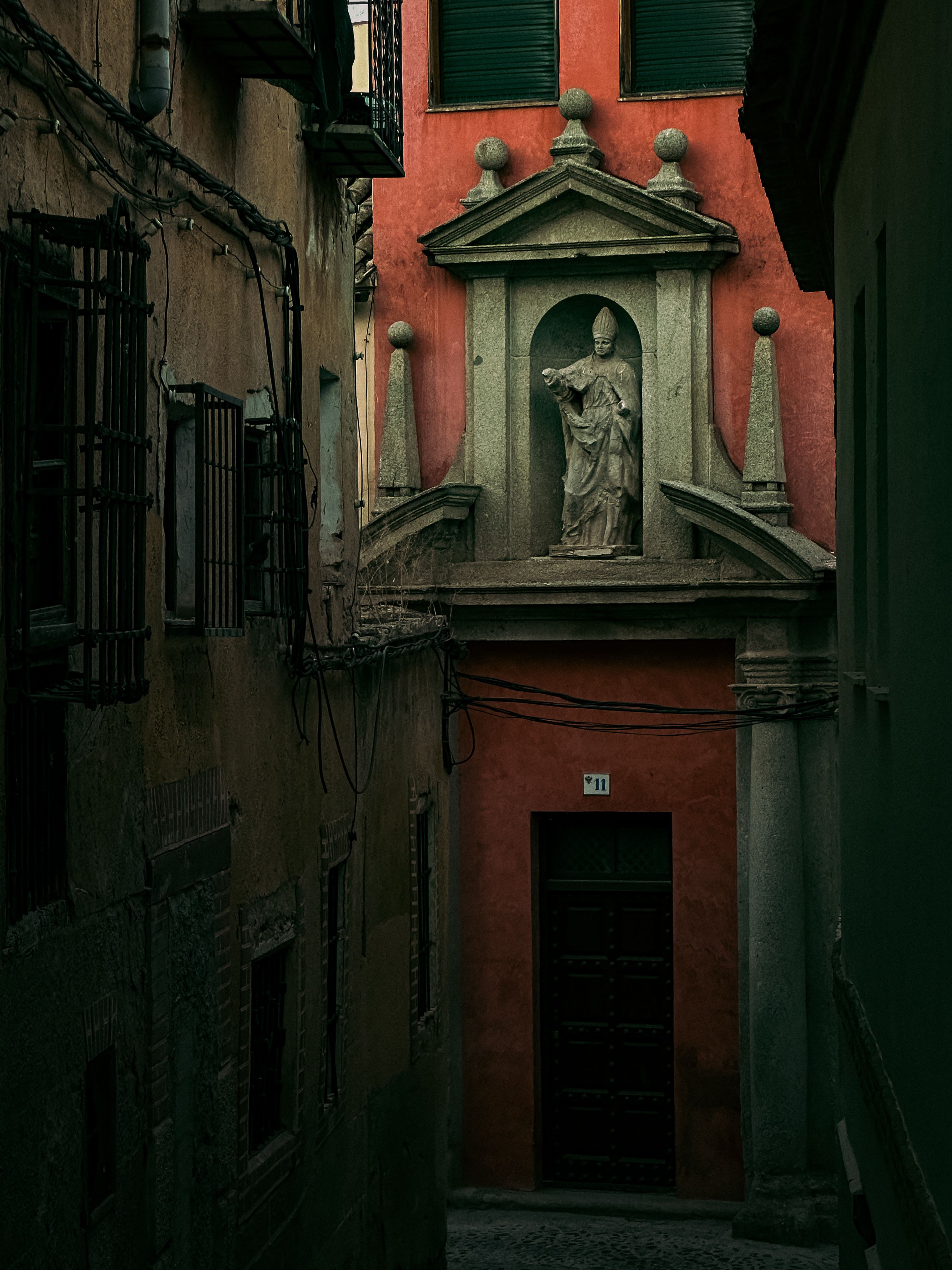 Dramatic view of a historic alleyway in Toledo, featuring ornate architecture and statue.