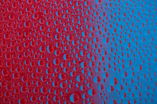 Free Close-up of water droplets on a vibrant red and blue surface showcasing abstract patterns. Stock Photo