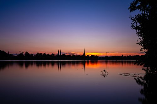 Free Peaceful sunset with silhouette of Lübeck's skyline reflected on calm waters. Stock Photo