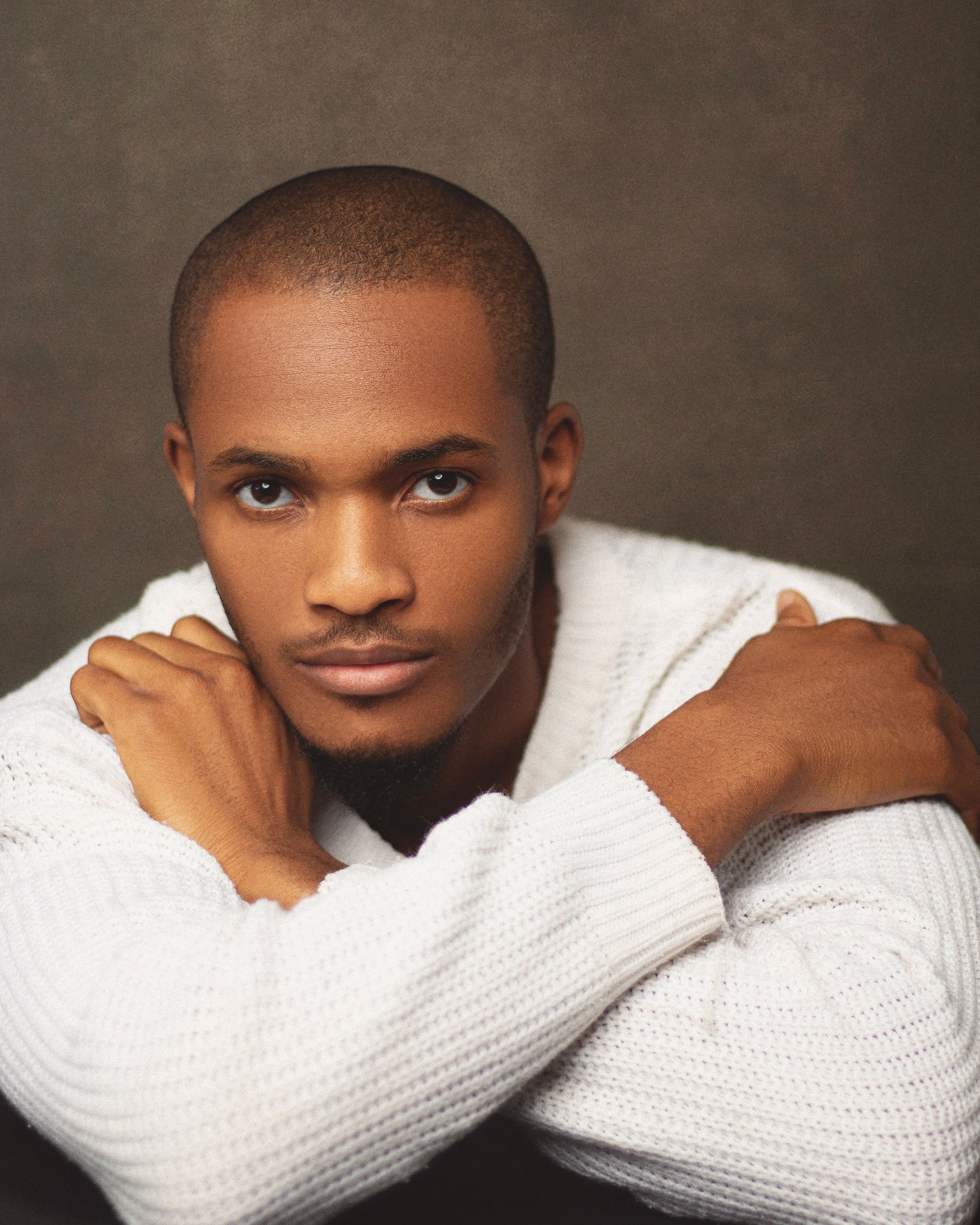 A thoughtful portrait of a man in a warm, white sweater laying his arms on his shoulders.
