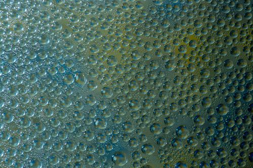 Free Intricate pattern of water droplets on glass with a blue and yellow background, creating a textured abstract effect. Stock Photo