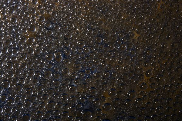 Gouttes d'eau formant des motifs abstraits sur surface sombre traitée hydrofuge