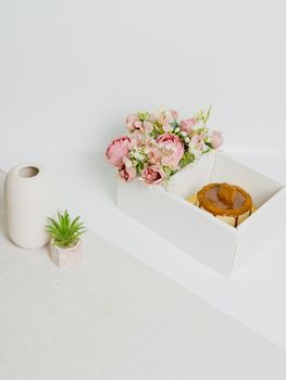 A stylish composition of pink roses and a cake in a white box.