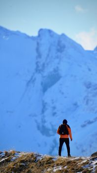 A lone hiker stands before a stunning snow-covered mountain in winter.