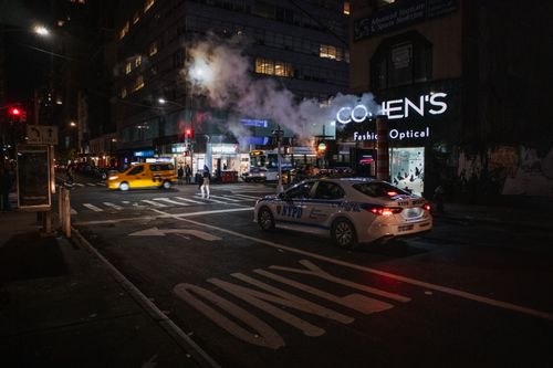 Free A vibrant NYC street at night featuring an NYPD car, a yellow cab, and illuminated storefronts. Stock Photo