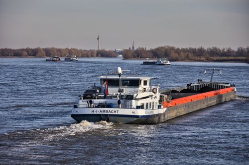 Free A cargo ship cruising along a wide river under a clear sky, showcasing inland waterway transport. Stock Photo