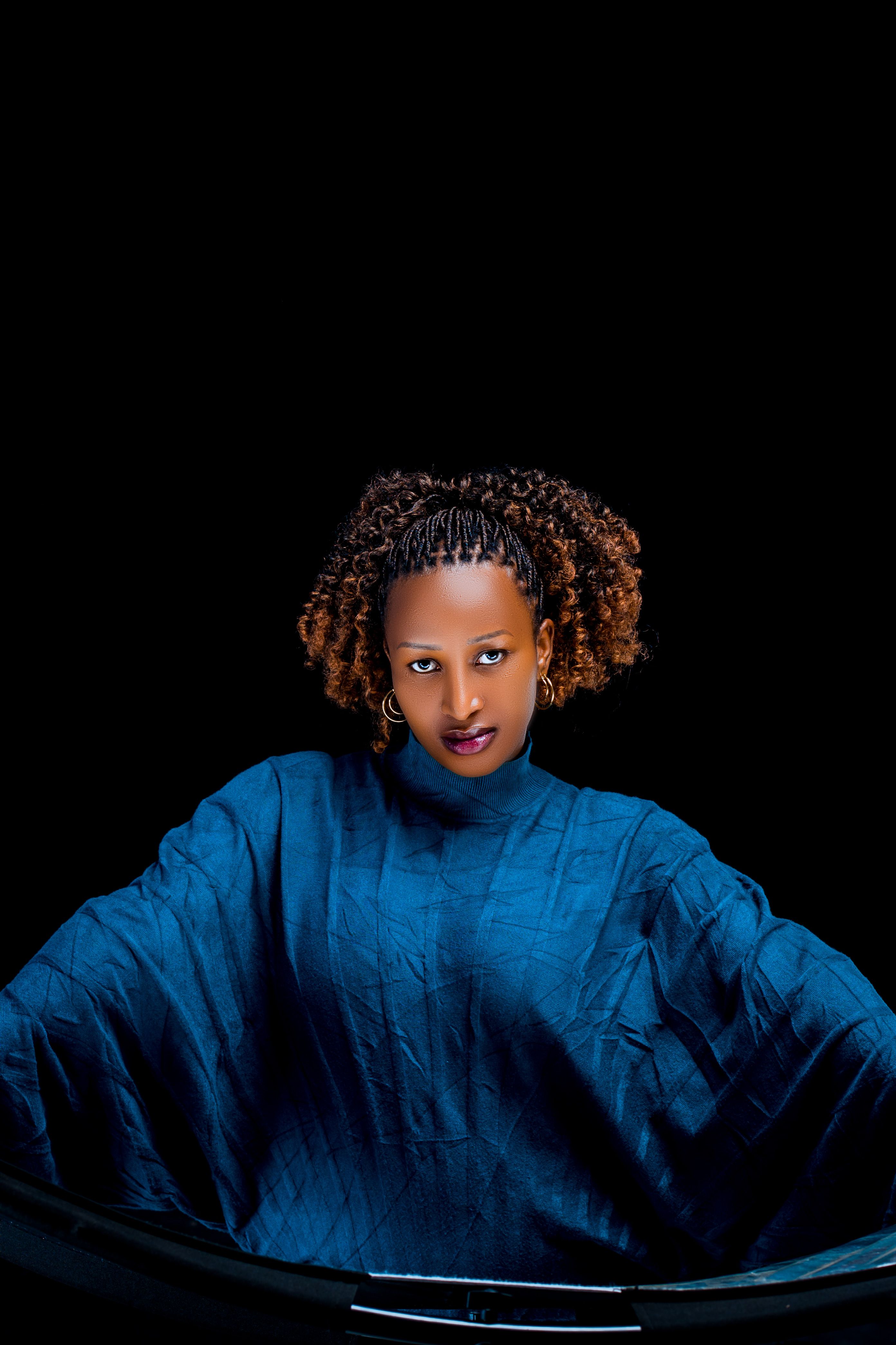 Striking portrait of a woman in blue clothing with a black background. High contrast and artistic style.