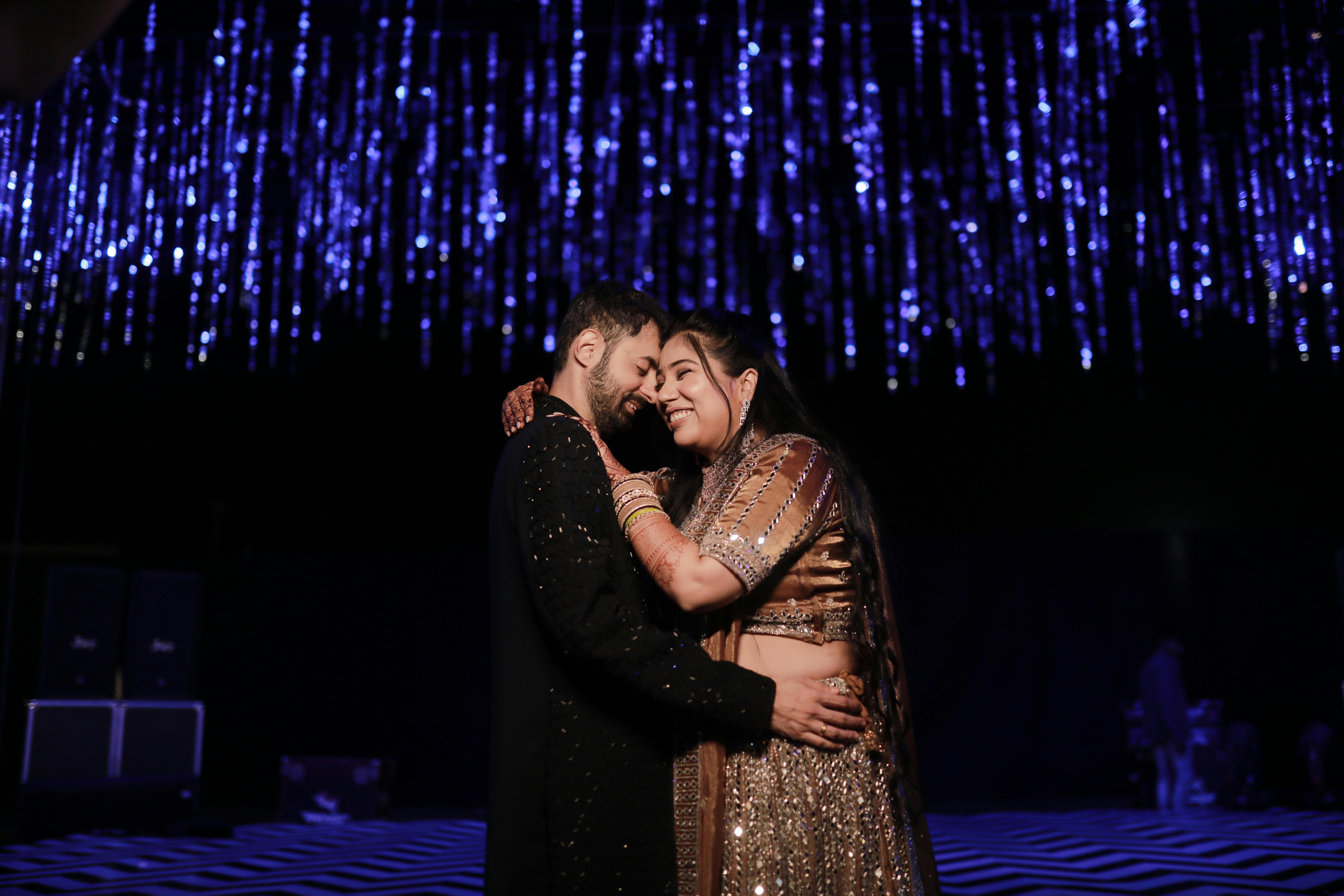 A couple embraces happily under shimmering blue lights, showcasing affection and joy.