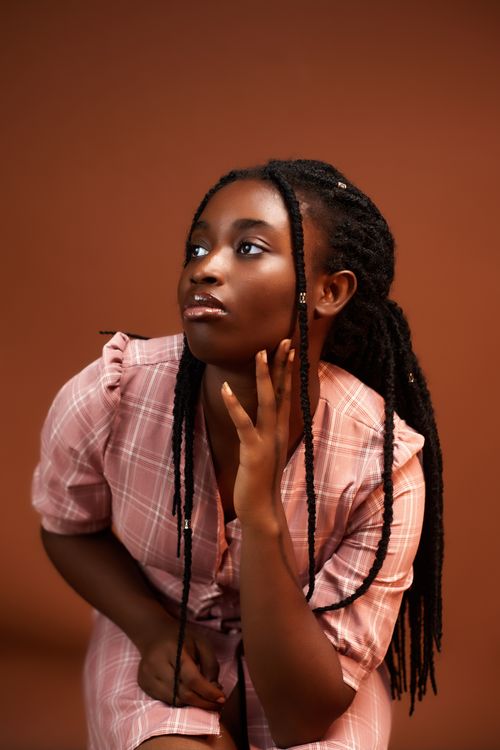 Free Portrait of a young woman in a plaid dress, looking contemplative against a brown background. Stock Photo
