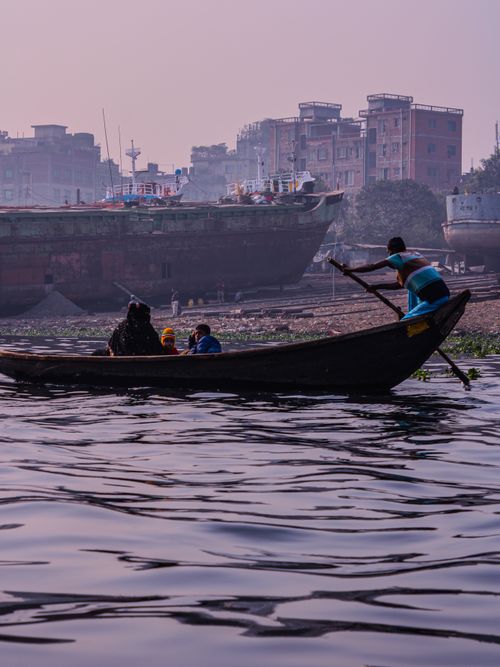 Free Rowing a traditional wooden boat on a river with urban background in Bangladesh. Stock Photo