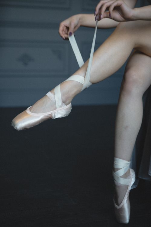 Free A graceful ballet dancer ties her pointe shoes, focusing on precision and elegance. Stock Photo